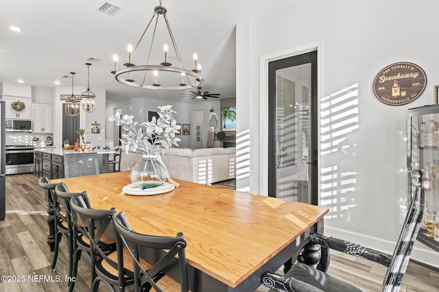 dining space with light wood-style flooring, recessed lighting, ceiling fan with notable chandelier, visible vents, and baseboards