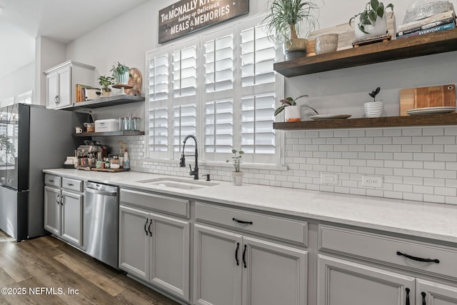 kitchen featuring dark wood-style floors, appliances with stainless steel finishes, a sink, open shelves, and backsplash