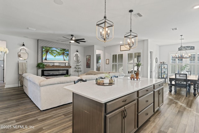 kitchen with dark wood-type flooring, a glass covered fireplace, open floor plan, and visible vents