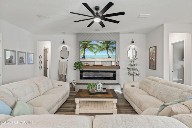 living area with ceiling fan, wood finished floors, a glass covered fireplace, and visible vents