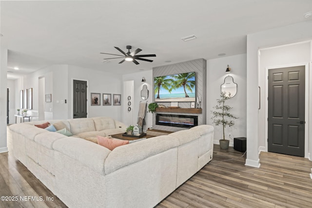 living area with baseboards, a ceiling fan, wood finished floors, and a glass covered fireplace