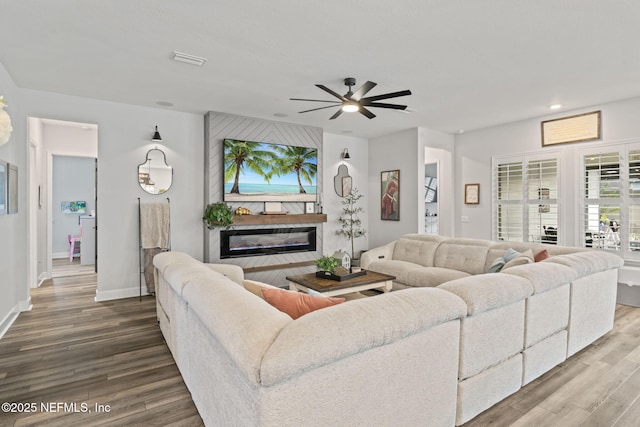 living room featuring baseboards, visible vents, wood finished floors, and a glass covered fireplace