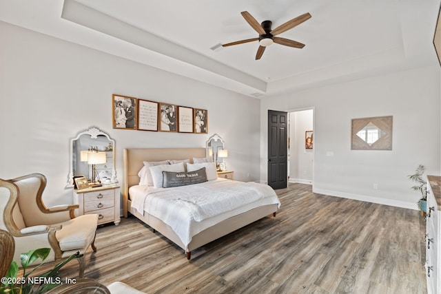 bedroom with light wood-style floors, a raised ceiling, ceiling fan, and baseboards