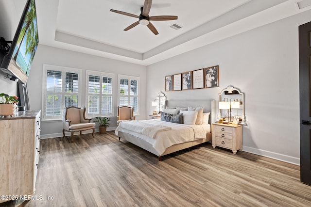 bedroom featuring light wood-style floors, baseboards, visible vents, and a raised ceiling