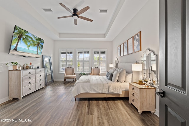 bedroom with baseboards, visible vents, a raised ceiling, and wood finished floors