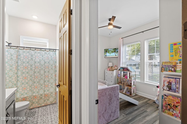 interior space with toilet, ceiling fan, vanity, wood finished floors, and a shower with curtain