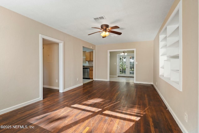 empty room with dark hardwood / wood-style floors, built in features, ceiling fan with notable chandelier, and french doors