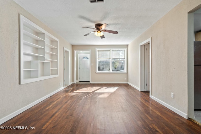 spare room featuring built in shelves, ceiling fan, dark hardwood / wood-style floors, and a textured ceiling