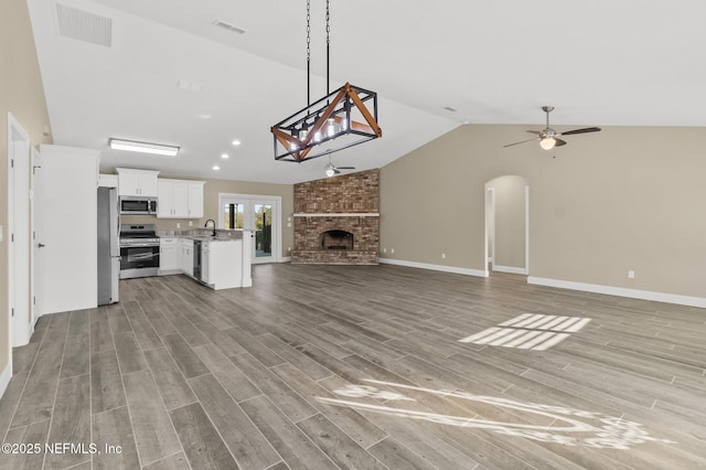 unfurnished living room with a brick fireplace, vaulted ceiling, ceiling fan, and sink