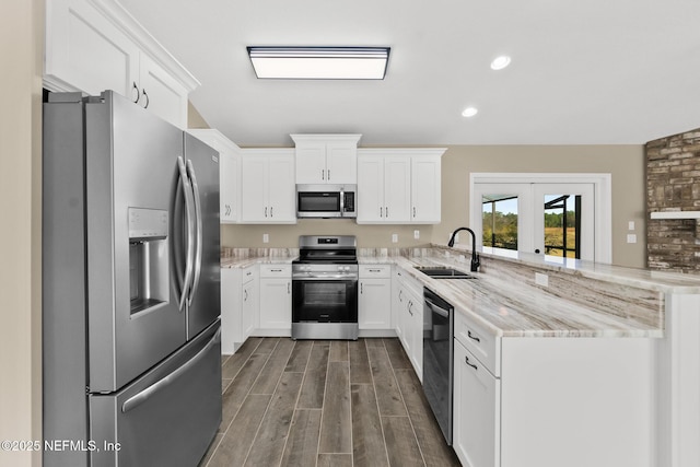 kitchen with white cabinetry, sink, light stone countertops, kitchen peninsula, and appliances with stainless steel finishes