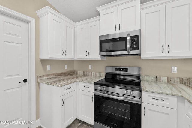 kitchen with white cabinets, appliances with stainless steel finishes, light stone counters, and dark wood-type flooring