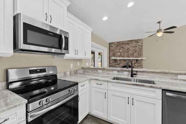 kitchen with light stone counters, stainless steel appliances, vaulted ceiling, sink, and white cabinets