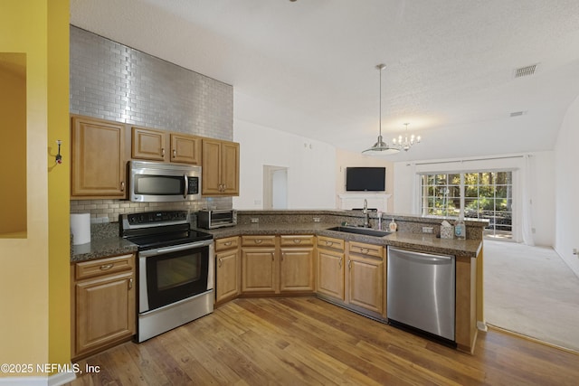 kitchen with an inviting chandelier, hanging light fixtures, sink, dark stone countertops, and appliances with stainless steel finishes