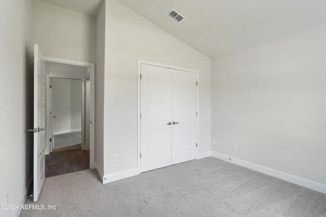 unfurnished bedroom with light carpet, a closet, and lofted ceiling