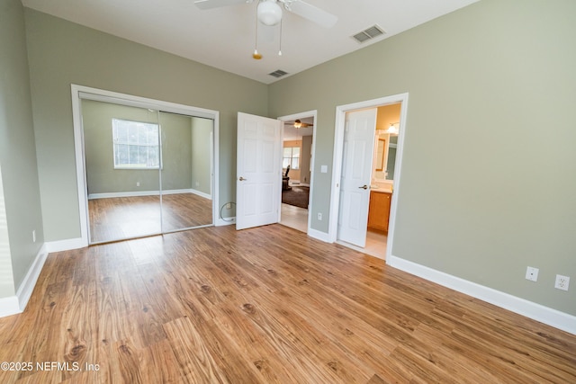 unfurnished bedroom featuring ceiling fan, light hardwood / wood-style floors, ensuite bathroom, and a closet