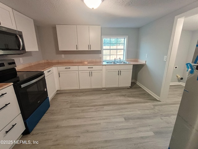 kitchen featuring stainless steel microwave, range with electric stovetop, a sink, and white cabinetry