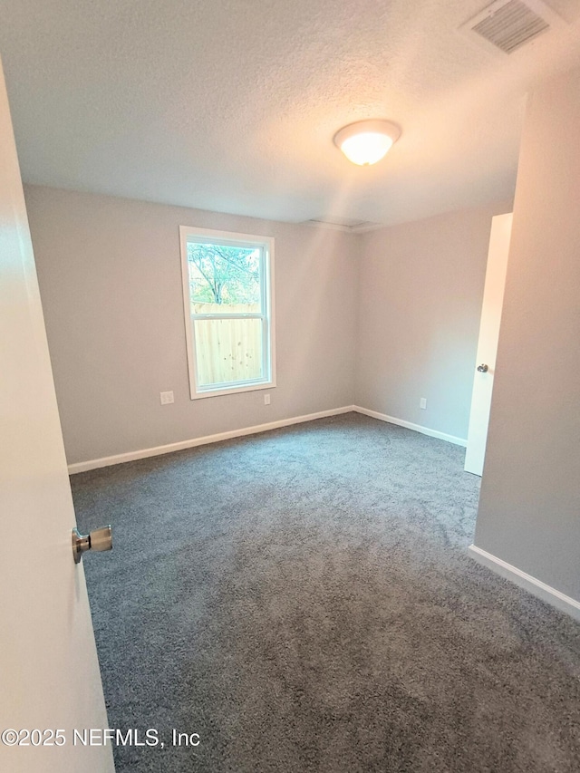 empty room featuring a textured ceiling, dark colored carpet, visible vents, and baseboards