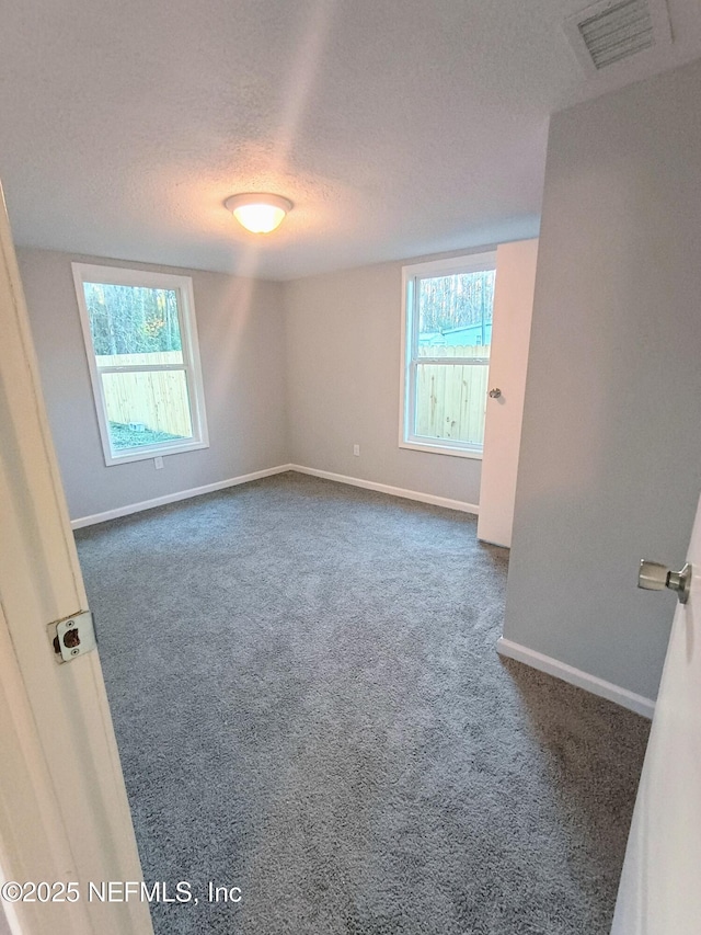 empty room featuring dark colored carpet, visible vents, a healthy amount of sunlight, and a textured ceiling