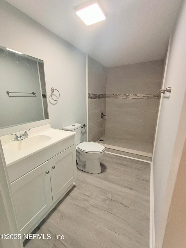 bathroom featuring toilet, vanity, wood finished floors, and tiled shower