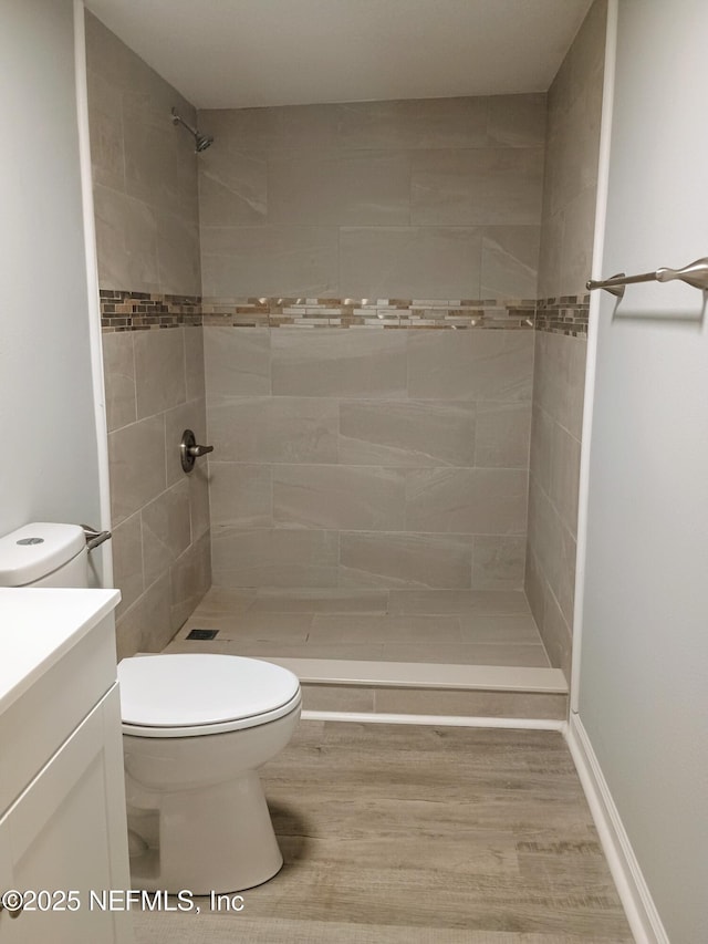 bathroom with toilet, a tile shower, wood finished floors, and vanity