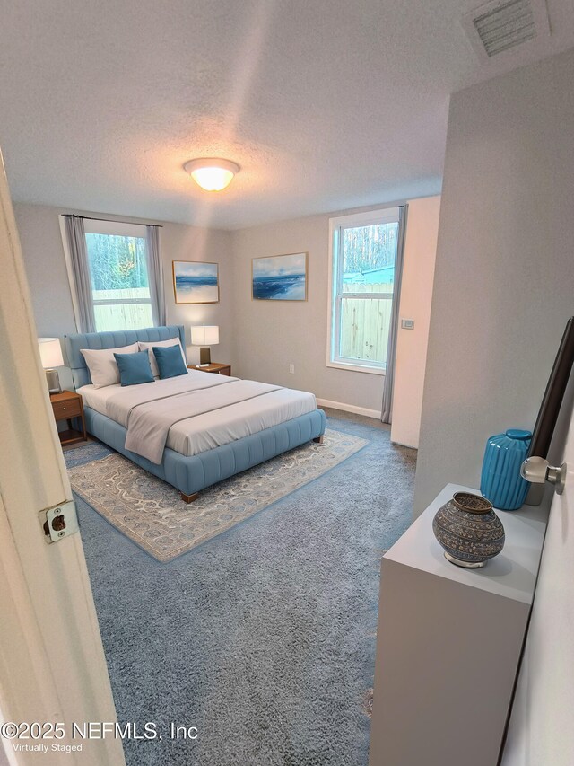 bedroom featuring a textured ceiling, carpet floors, multiple windows, and visible vents