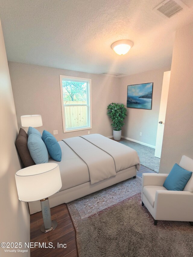 bedroom with visible vents, a textured ceiling, baseboards, and wood finished floors