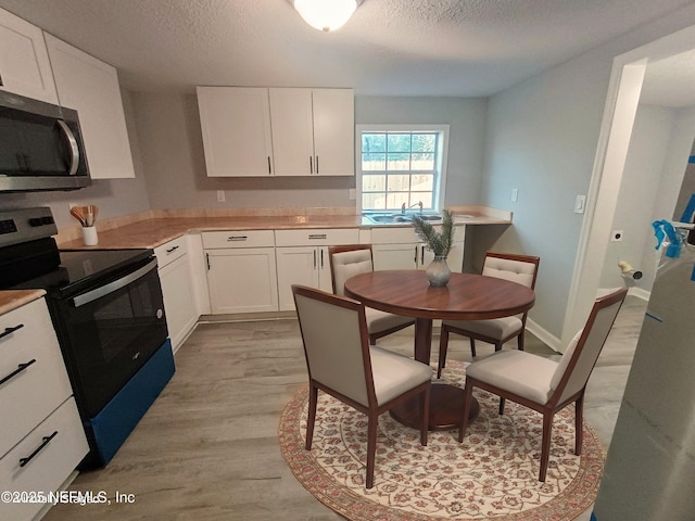 kitchen with stainless steel microwave, electric range oven, white cabinetry, a textured ceiling, and light wood-type flooring