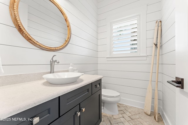 bathroom with toilet, vanity, and wood walls