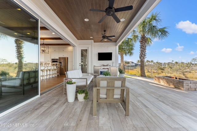 wooden deck featuring ceiling fan and an outdoor living space with a fire pit