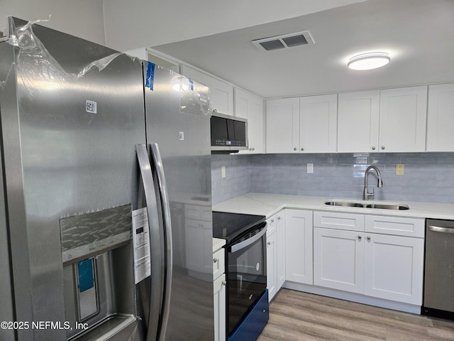 kitchen featuring white cabinetry, sink, stainless steel appliances, tasteful backsplash, and light wood-type flooring