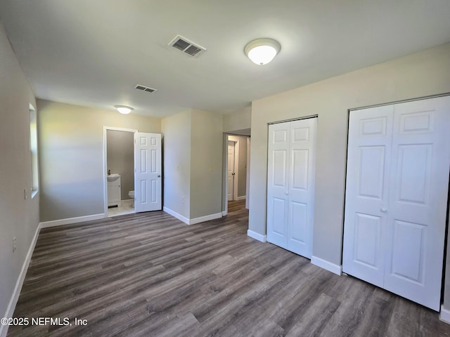 unfurnished bedroom featuring ensuite bathroom, dark wood-type flooring, and two closets