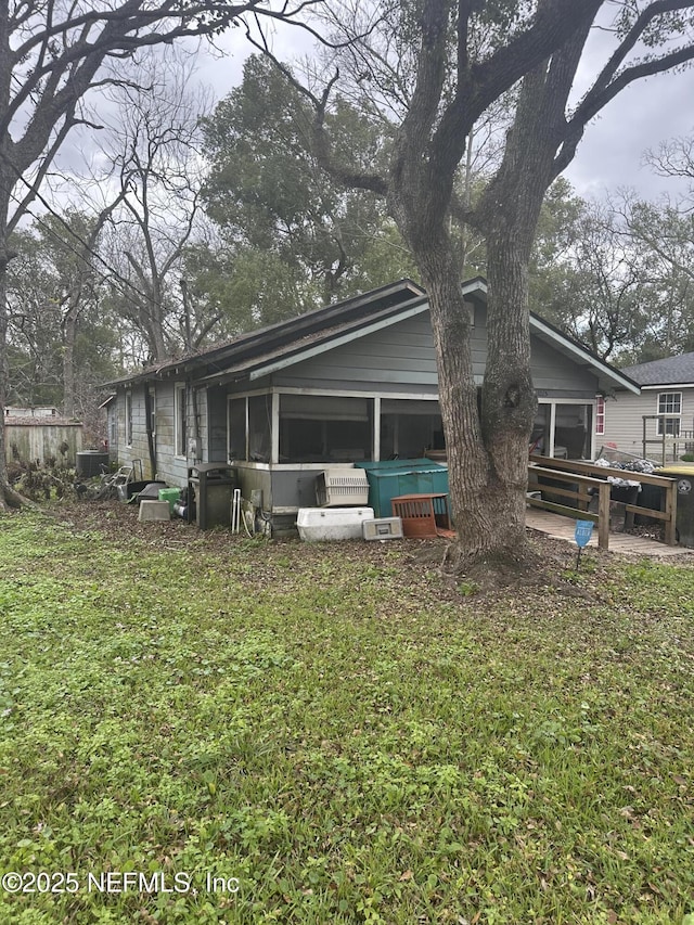 rear view of property with a jacuzzi, a sunroom, and a lawn