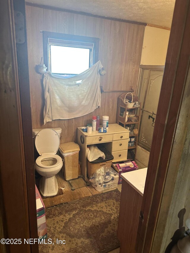 bathroom with a textured ceiling, vanity, wooden walls, wood-type flooring, and toilet