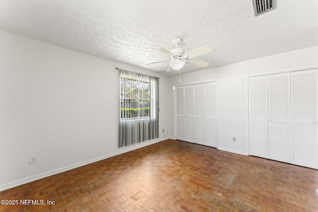 unfurnished bedroom featuring multiple closets, a textured ceiling, dark parquet floors, and ceiling fan