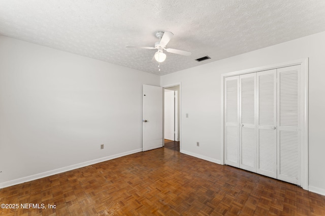 unfurnished bedroom with a textured ceiling, dark parquet floors, a closet, and ceiling fan