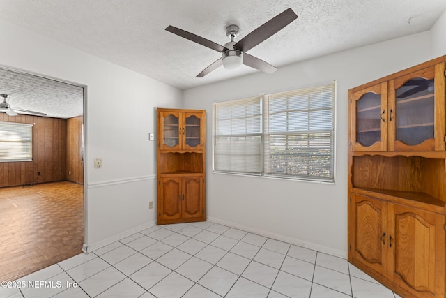 empty room with ceiling fan, a textured ceiling, and wooden walls