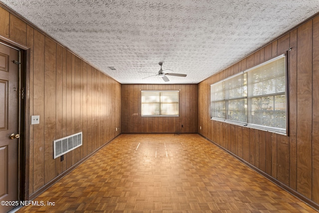 spare room with ceiling fan, parquet flooring, and wooden walls