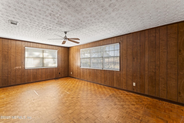 empty room featuring parquet floors, a textured ceiling, and wood walls