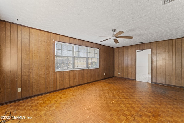 spare room featuring a textured ceiling, wooden walls, and light parquet floors