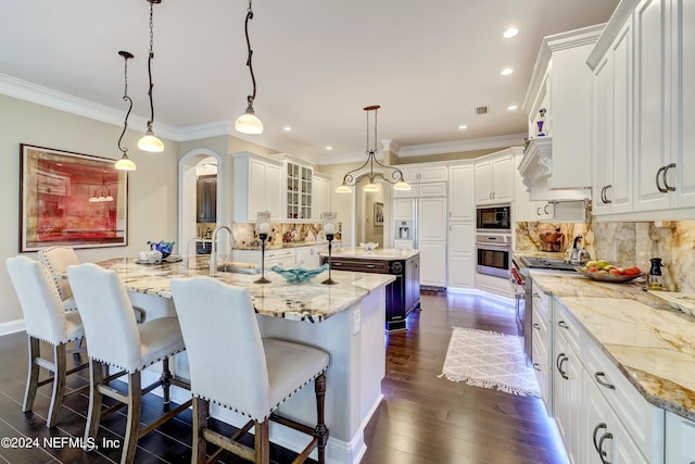 kitchen featuring a breakfast bar, hanging light fixtures, glass insert cabinets, white cabinetry, and a large island with sink