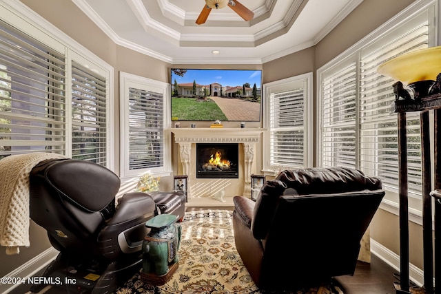 interior space with baseboards, a raised ceiling, a ceiling fan, a premium fireplace, and ornamental molding