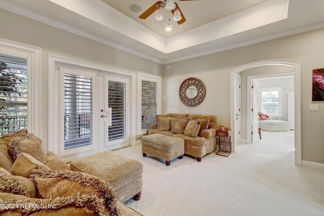 living room with arched walkways, light carpet, french doors, ornamental molding, and a tray ceiling