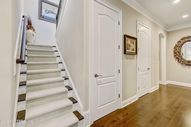 stairway featuring baseboards, arched walkways, ornamental molding, wood finished floors, and recessed lighting