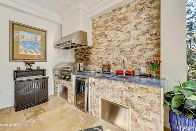 kitchen featuring wine cooler, a sink, wall chimney exhaust hood, stone finish floor, and dark countertops