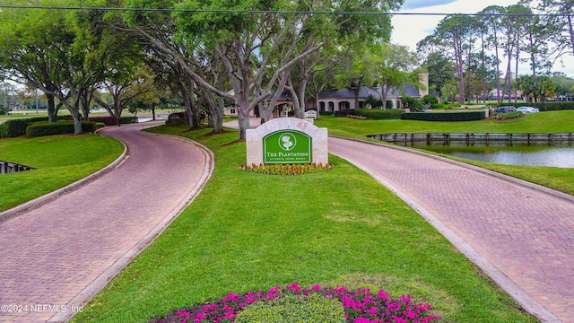 view of community with a water view, decorative driveway, and a lawn