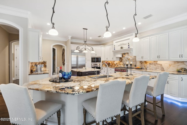 kitchen featuring pendant lighting, light stone countertops, a center island with sink, and white cabinets