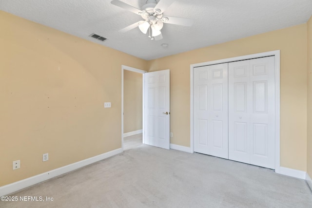 unfurnished bedroom with light carpet, ceiling fan, a closet, and a textured ceiling