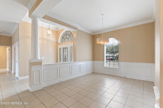 tiled empty room with ornamental molding, decorative columns, and a textured ceiling