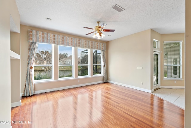 spare room with ceiling fan, a water view, a textured ceiling, and light wood-type flooring