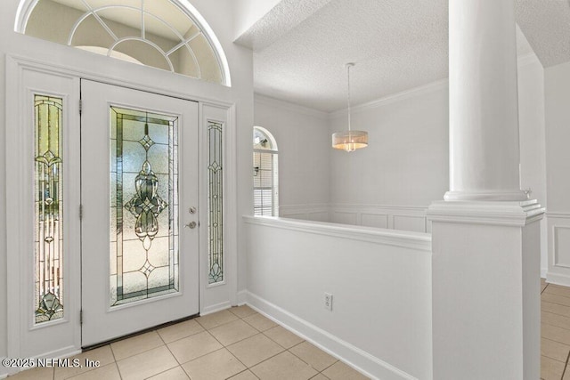 entryway with light tile patterned floors, ornate columns, a textured ceiling, crown molding, and a decorative wall